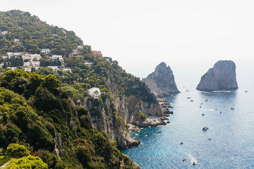 A coastal town with buildings on a hillside, rocky cliffs, and boats in the water. 1