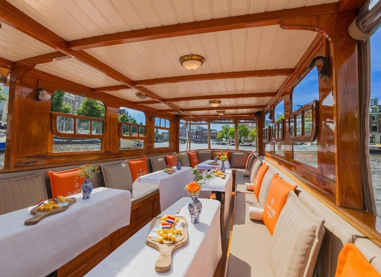A boat interior with wooden beams, tables with white tablecloths, and orange cushions. 1
