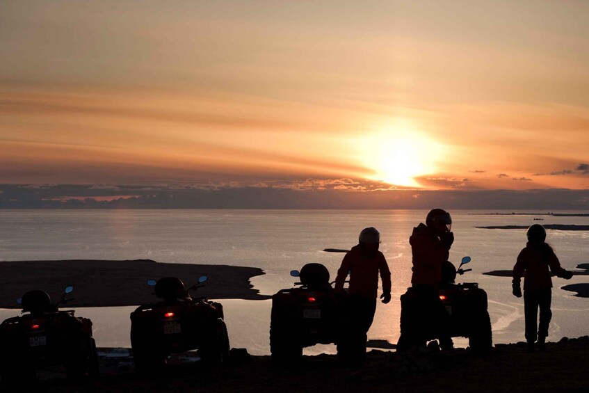 A sunset over a body of water with people and ATVs on the shore. 4