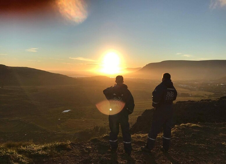 Two people standing on a hill overlooking a valley with the sun setting in the background. 3