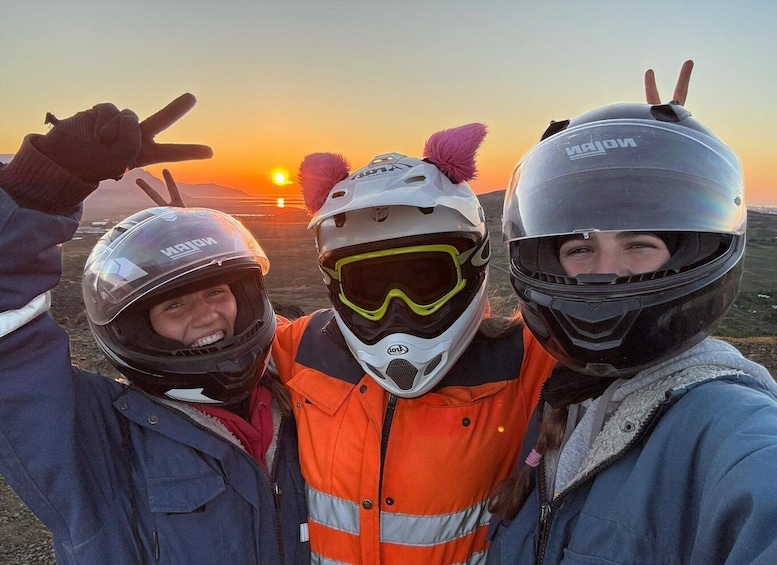Three people wearing helmets and jackets, with a sunset in the background. 1