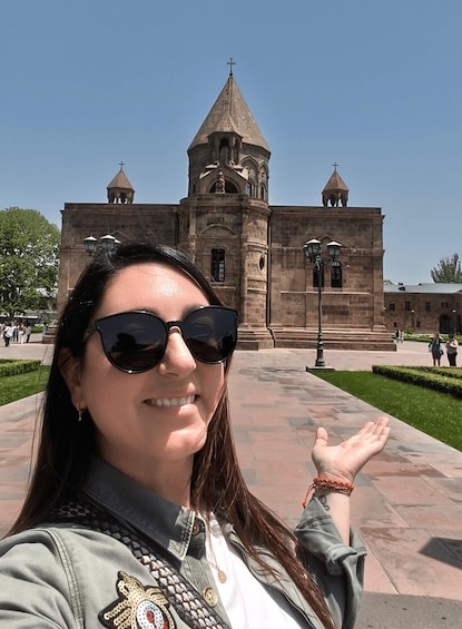 A woman taking a selfie in front of a historic building with a tall tower and multiple smaller towers. 3