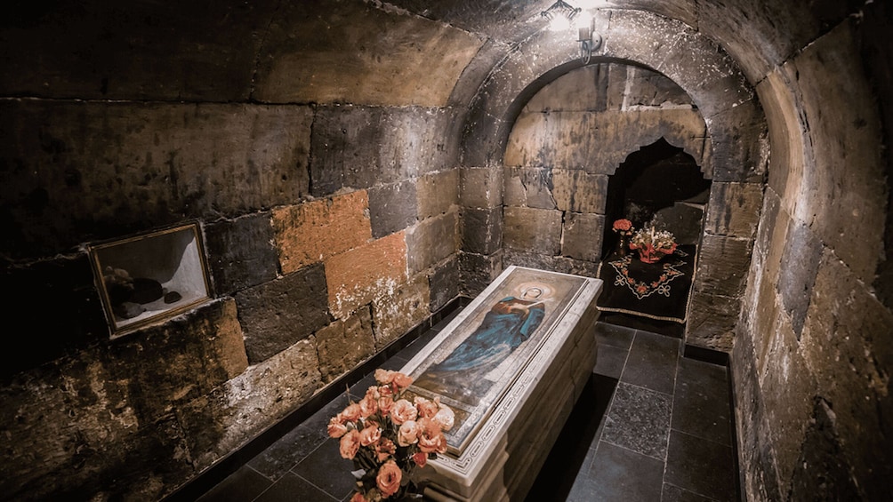 An ancient tomb with a sarcophagus, stone walls, and a floral arrangement. 4