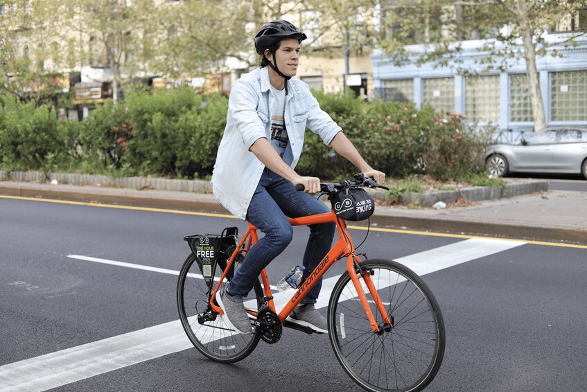 Una persona montando en bicicleta con una cesta trasera, usando casco y una camisa de color claro. 3