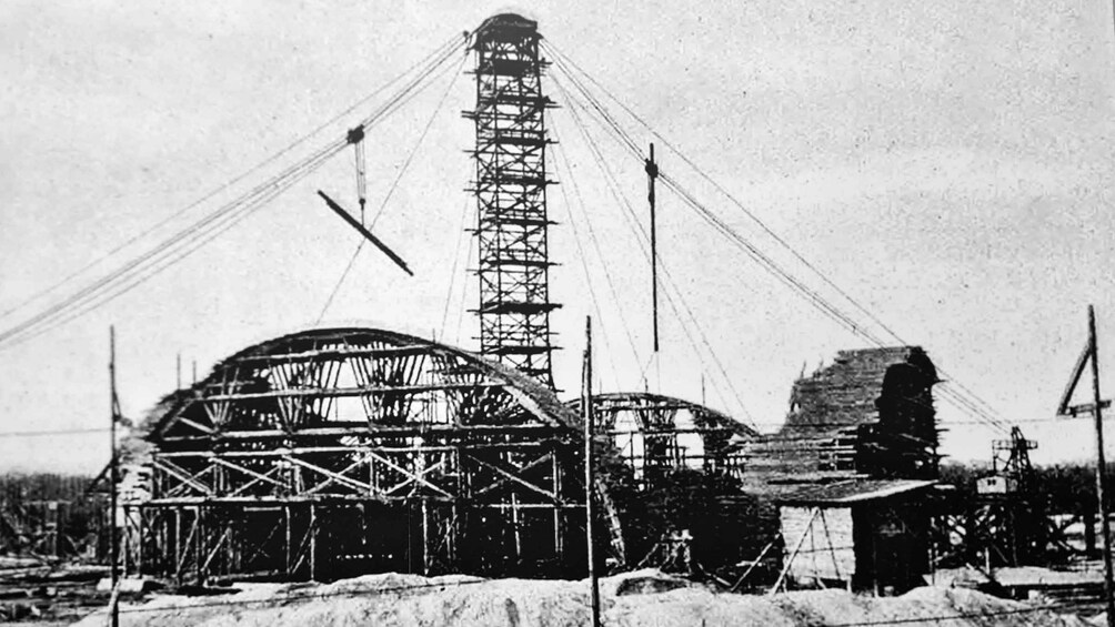 A large, partially constructed building with a central tower and multiple supporting cables. 2