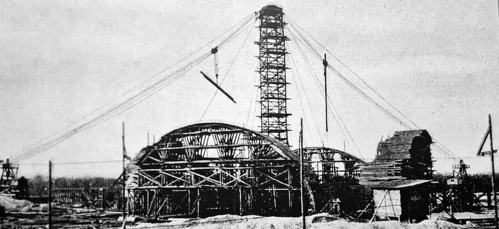 Un grand bâtiment industriel, doté d’une haute cheminée, entouré d’échafaudages et de matériaux de construction. 2