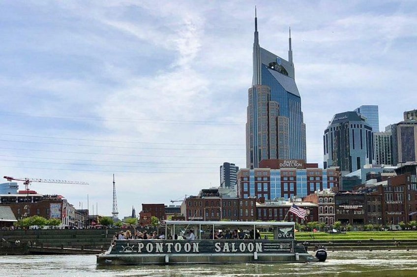 A riverboat named PONTOON SALOON on a river with a city skyline in the background. 1