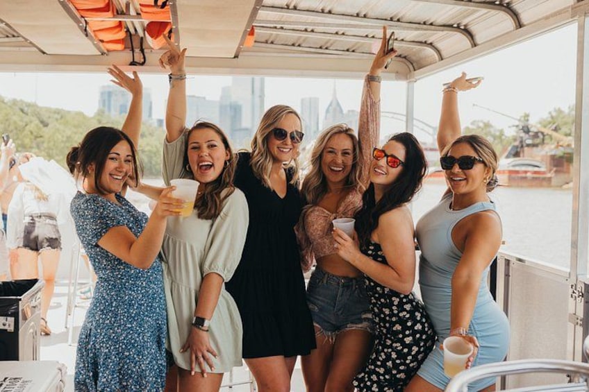 A group of people on a boat, some holding drinks, with a city skyline in the background. 2