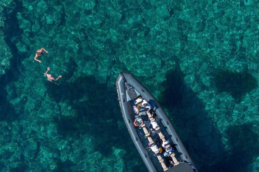 Vista aérea de un barco con gente a bordo y dos personas nadando en agua cristalina. 2