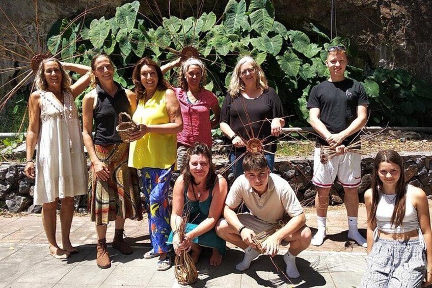 A group of people outdoors, some holding objects, with large green leaves in the background. 4