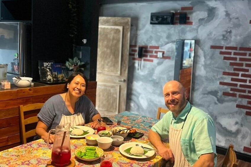 Two people sitting at a table with food and drinks, in a room with a brick wall and a window. 2