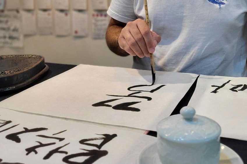A person writing calligraphy on paper with a brush, a ceramic jar, and calligraphy paper on a table. 2