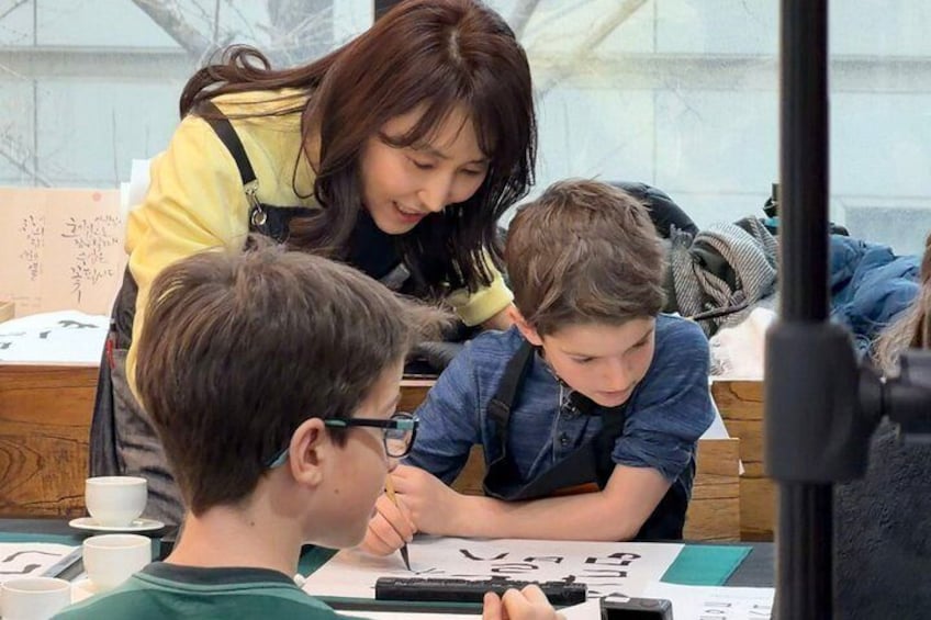 Une personne qui enseigne à un enfant, assis à une table avec du matériel d’écriture. 1