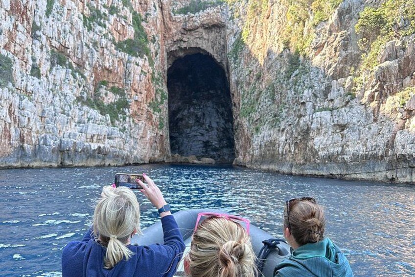 Three people on a boat near a rocky coastline with a cave-like formation. 2