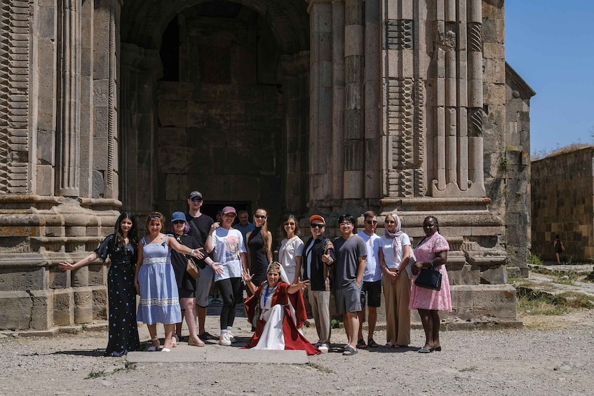 Un gruppo di persone in piedi di fronte a un antico edificio in pietra con colonne e archi. 1