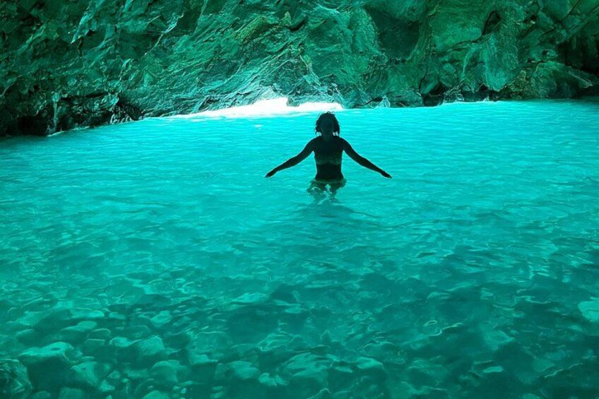 A person standing in clear turquoise water with rocky cave walls in the background. 2