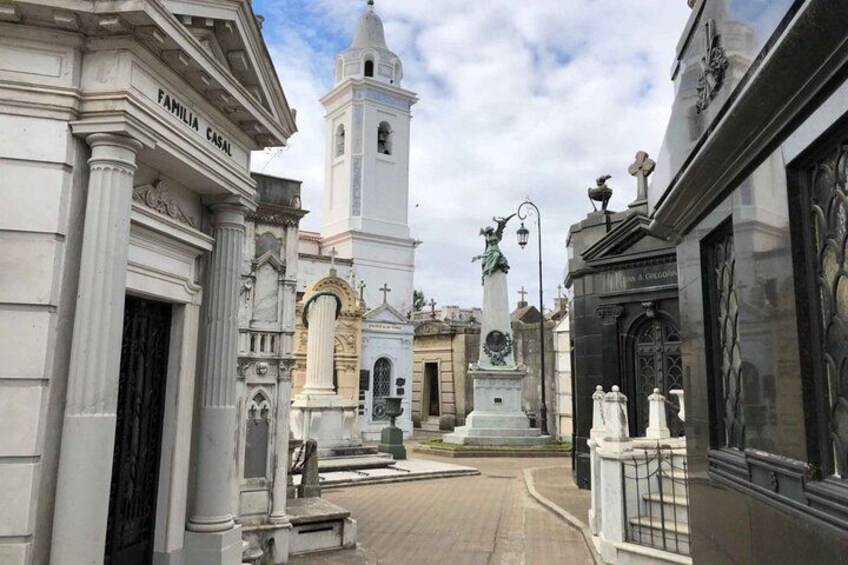 A street with buildings, a white church with a bell tower, and a statue in the center. 4