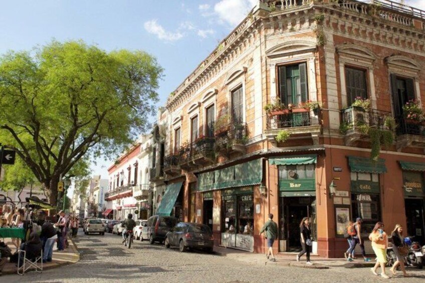 A cobblestone street lined with historic buildings, a tree, and pedestrians. 5