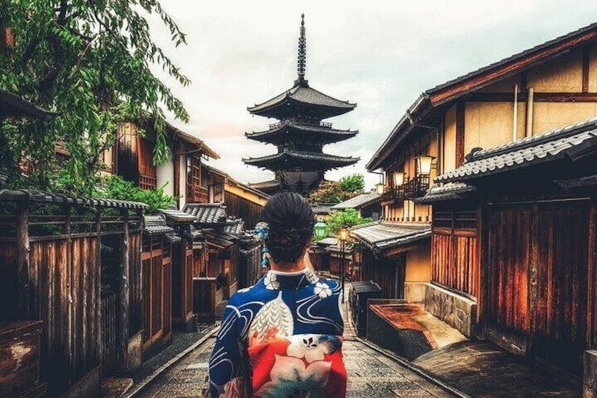 En traditionel japansk gade med træbygninger, en pagode og en person i kimono. 1