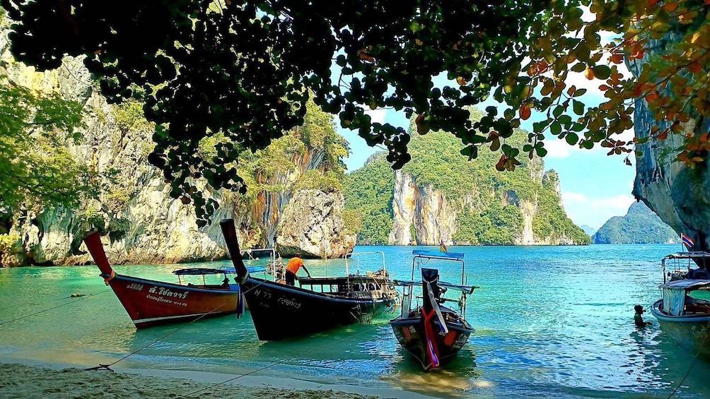 Three boats docked at a beach with clear turquoise water and rocky cliffs in the background. 2