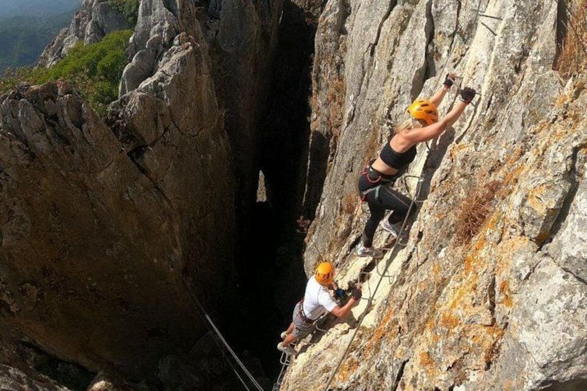Two people rock climbing on a steep rock face with a narrow passage between them. 1