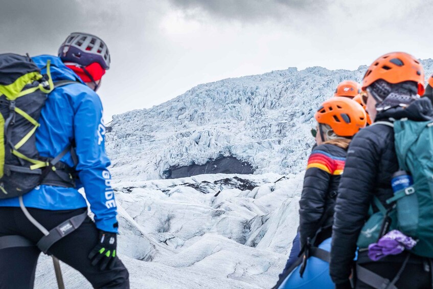 A group of people wearing helmets and backpacks, standing on a snowy mountain with a glacier in the background. 1