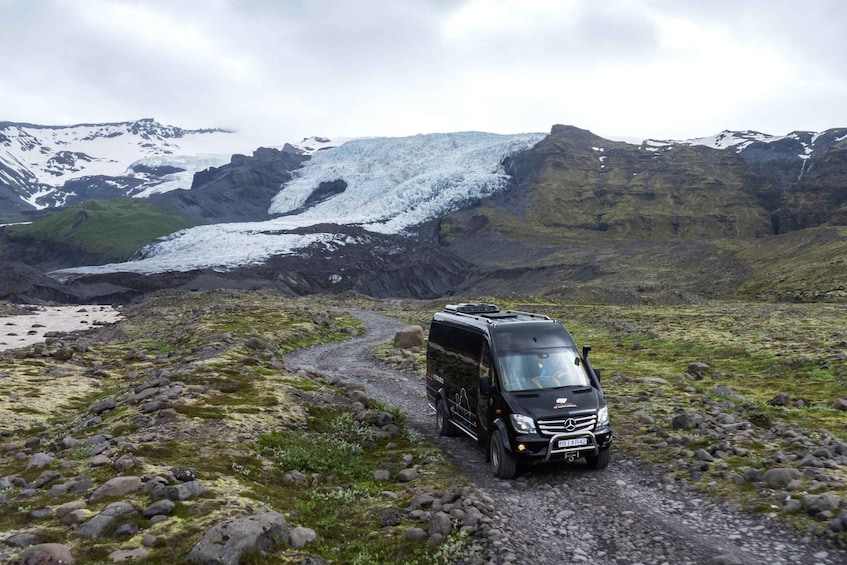 A black Mercedes-Benz camper van on a rocky path with snow-capped mountains in the background. 5