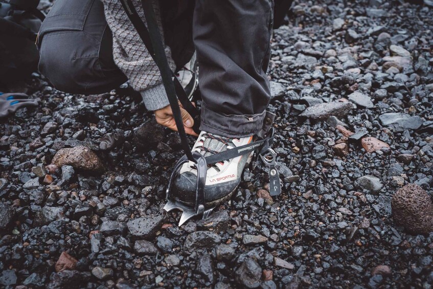 A person adjusting a shoe with a strap on a rocky surface. 3