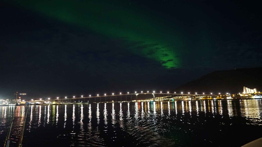 A bridge at night with lights reflecting on water, and the aurora borealis in the sky. 2