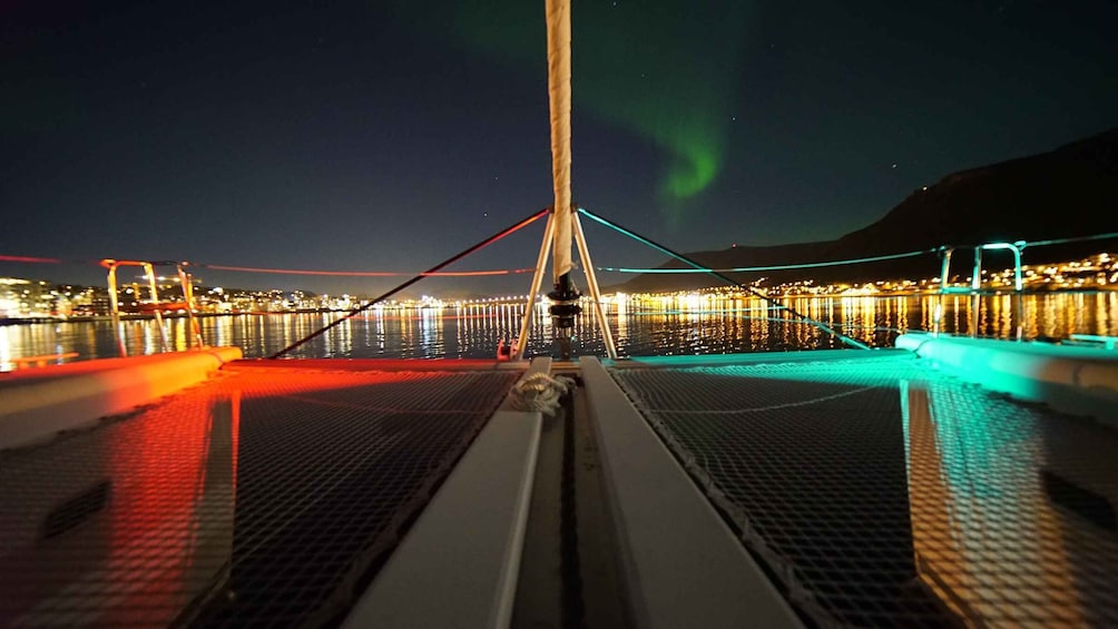 A nighttime view from a boat with a cityscape in the background, illuminated by colorful lights. 1