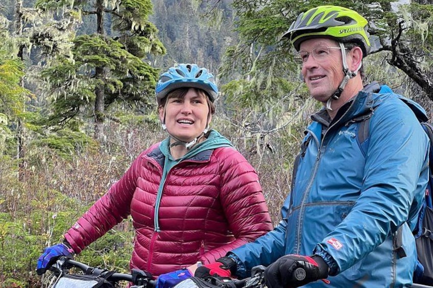 Two people wearing helmets and jackets, standing near a mountain. 2