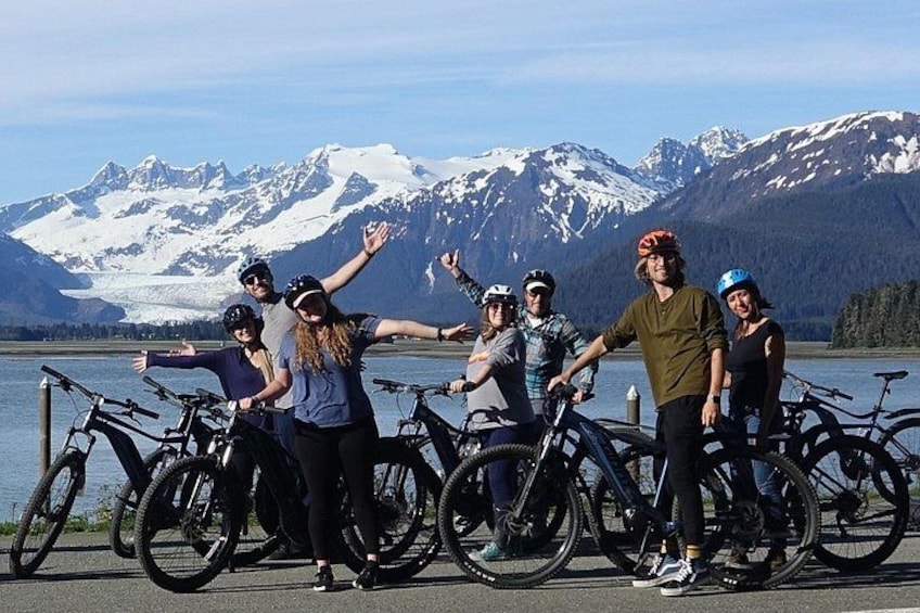 A group of people with bicycles by a lake with mountains in the background. 5