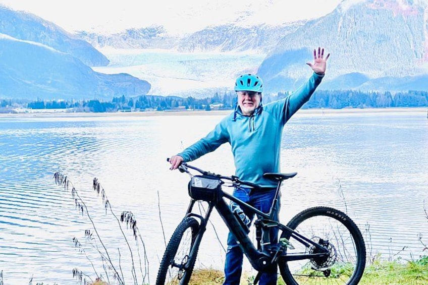 A person on a mountain bike by a lake with mountains in the background. 4