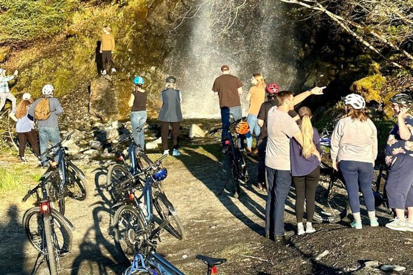 A group of people standing by a waterfall, some with bicycles. 3