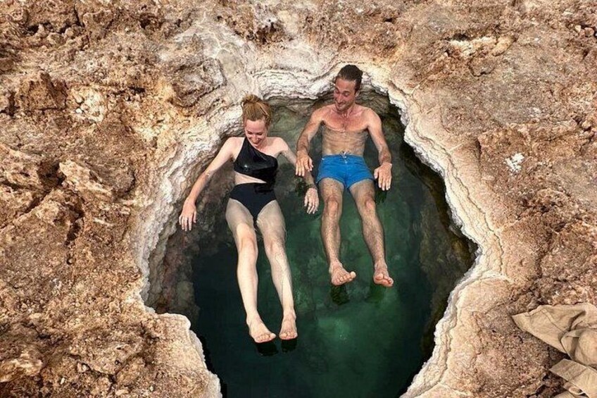 Two people floating in a natural water-filled crevice surrounded by rocky terrain. 3