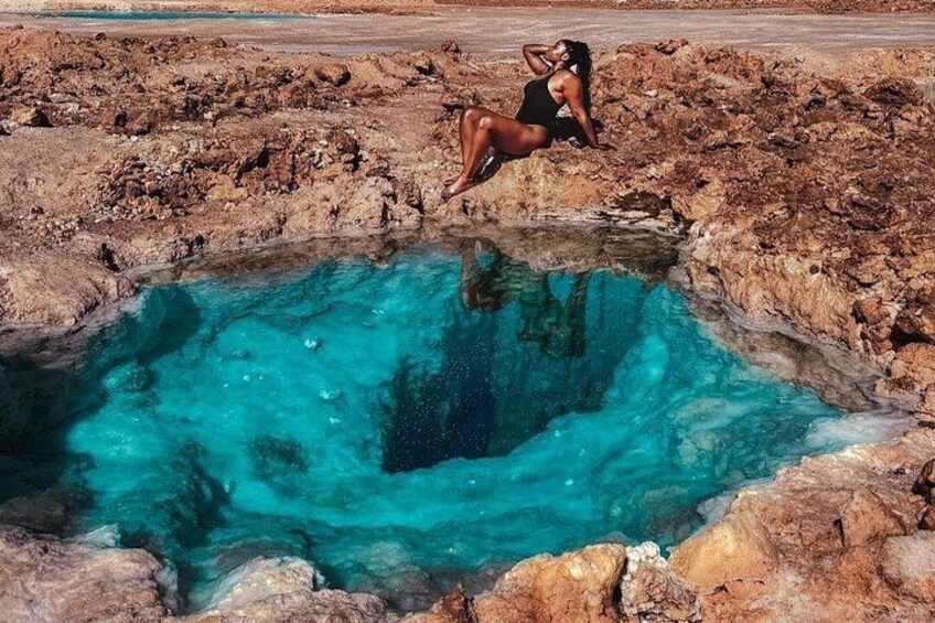 A person sitting on a rocky ledge by a turquoise pool. 2
