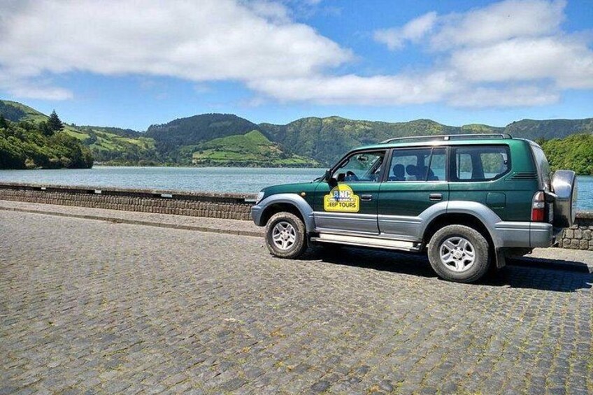 Un VUS vert est garé sur un chemin pavé de pierres, près d’un lac, avec des montagnes en arrière-plan. 1