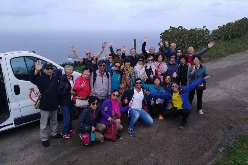 A group of people posing with a van on a road with a body of water in the background. 4