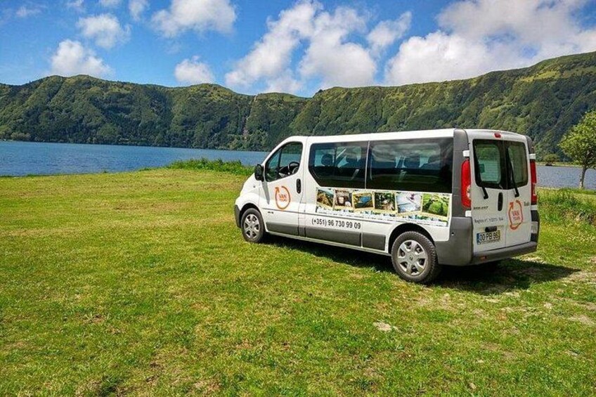 A white van parked on a grassy field with a lake and mountains in the background. 2