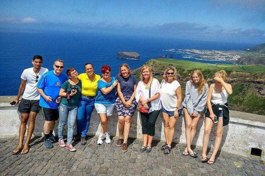 A group of people standing on a stone path with a coastal landscape in the background. 3