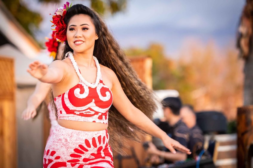A person in a red and white patterned outfit with a flower in their hair, dancing outdoors. 1