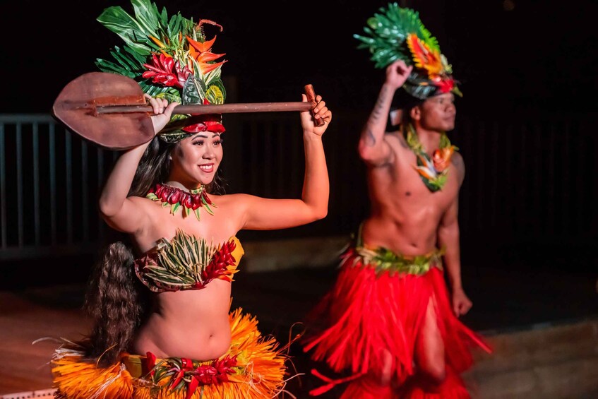 Two performers in traditional Hawaiian attire with feathered headdresses and skirts, holding props. 4