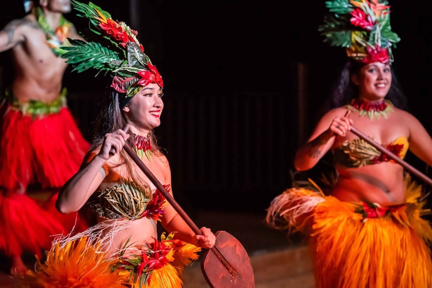 Two dancers in traditional Hawaiian costumes performing a dance with a wooden paddle. 5
