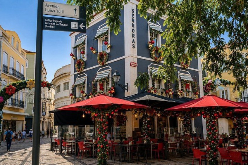 Sitzgelegenheiten im Freien mit roten Sonnenschirmen, ein Gebäude mit festlicher Dekoration und ein Wegweiser mit Beschilderung. 3