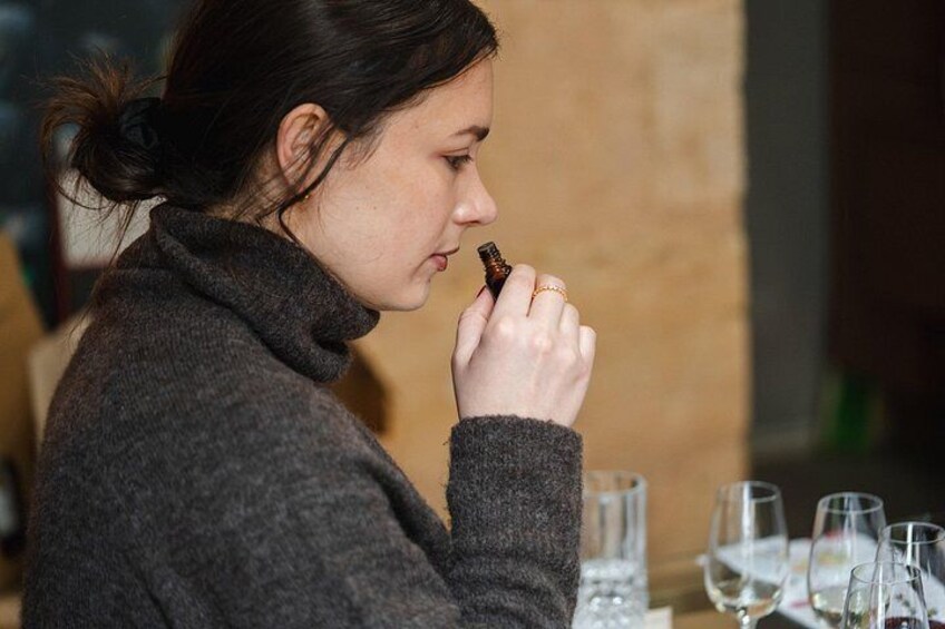 A person holding a small bottle, possibly a perfume or cologne, at a table with glasses and a bottle. 5