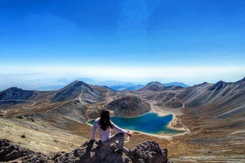A person sitting on a rocky outcrop overlooking a lake surrounded by mountains. 1