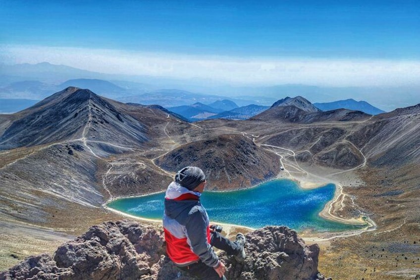 A person sitting on a rocky outcrop overlooking a lake surrounded by mountains. 2
