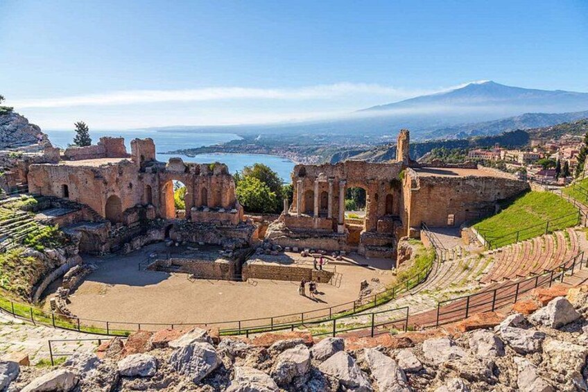 Ancient ruins with a large amphitheater, a stone pathway, and a distant mountain. 1