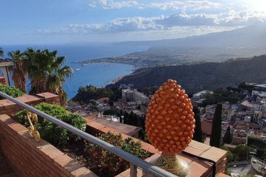 A coastal cityscape with a prominent orange sculpture on a balcony, palm trees, and a view of the sea and distant mountains. 5