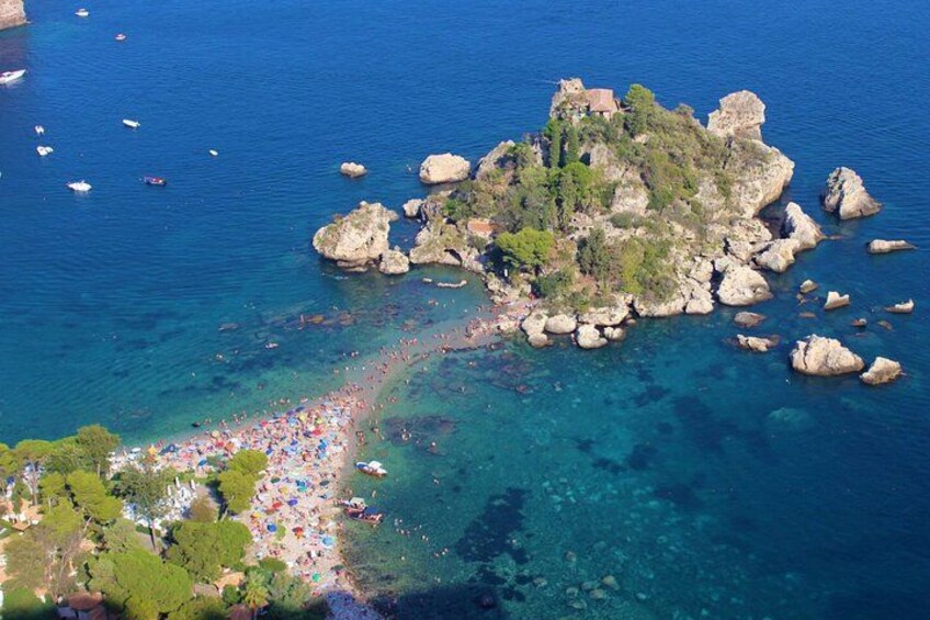 A coastal area with a rocky island, clear blue waters, and a crowded beach. 2